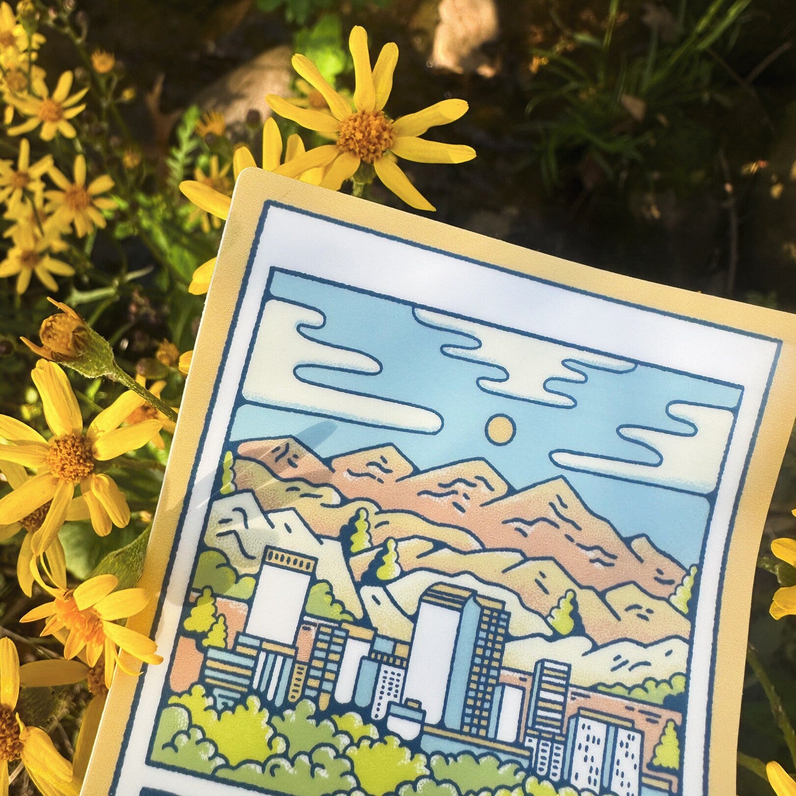 Illustrated card with a cityscape and mountains surrounded by yellow flowers