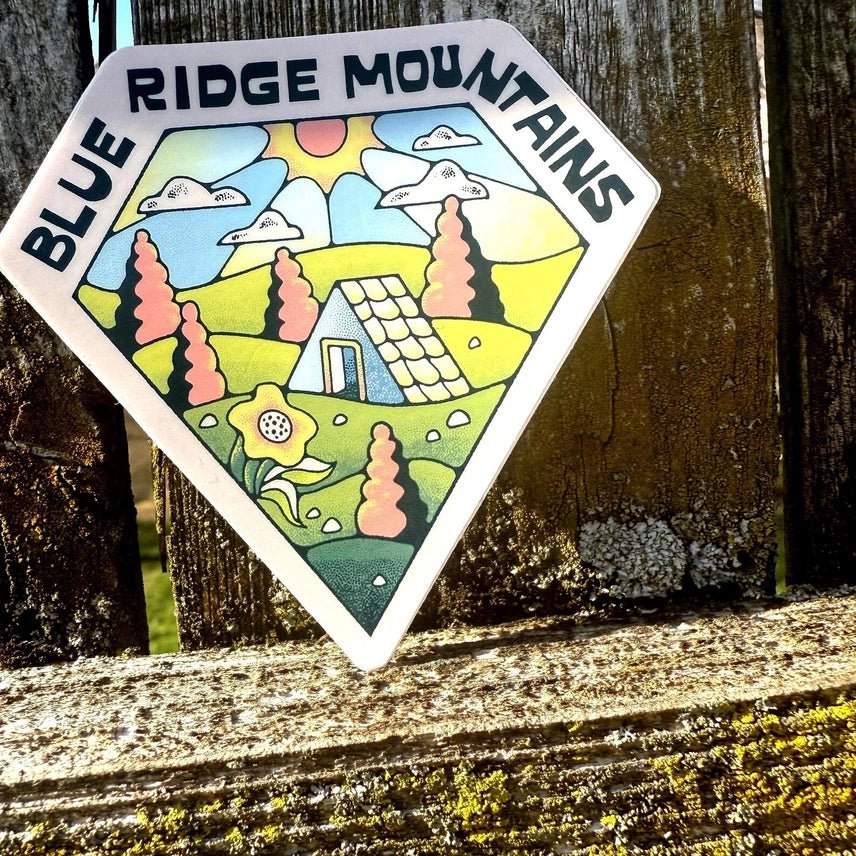 Sticker with cartoon mountain and text 'Blue Ridge Mountains' on wooden surface.