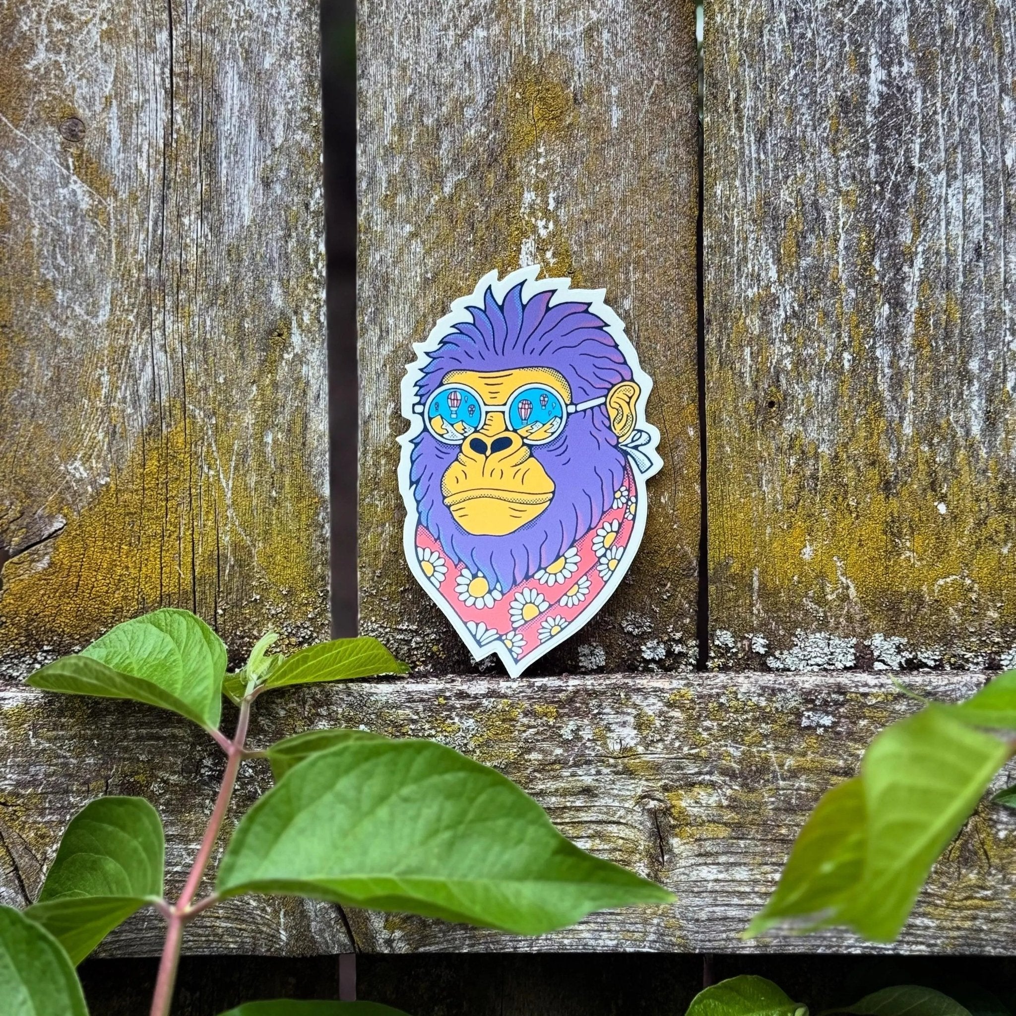 Colorful sticker of a stylized monkey with sunglasses on a wooden surface with green leaves.
