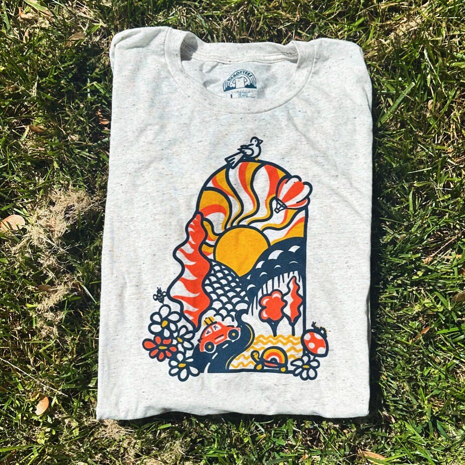 A t-shirt with a colorful mountain and sun design laid out on the grass.