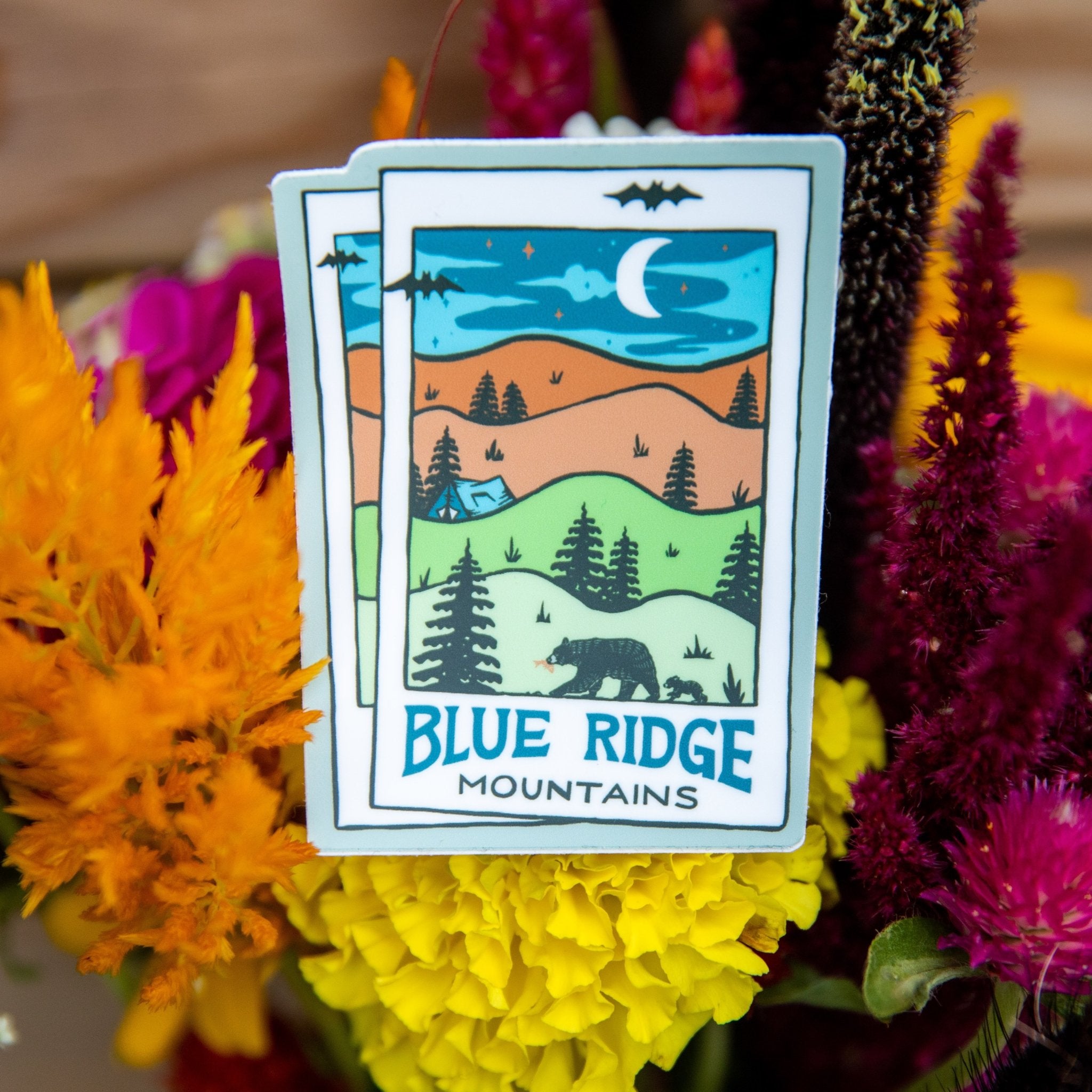 A vinyl sticker with a Blue Ridge Mountains design, featuring a moonlit landscape with trees and a cabin under the moon and stars.