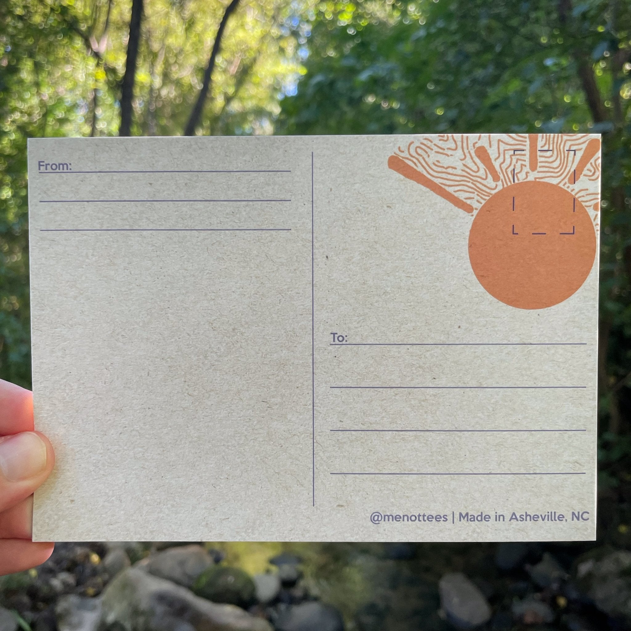 Postcard held in wooded outdoor setting with trees in background