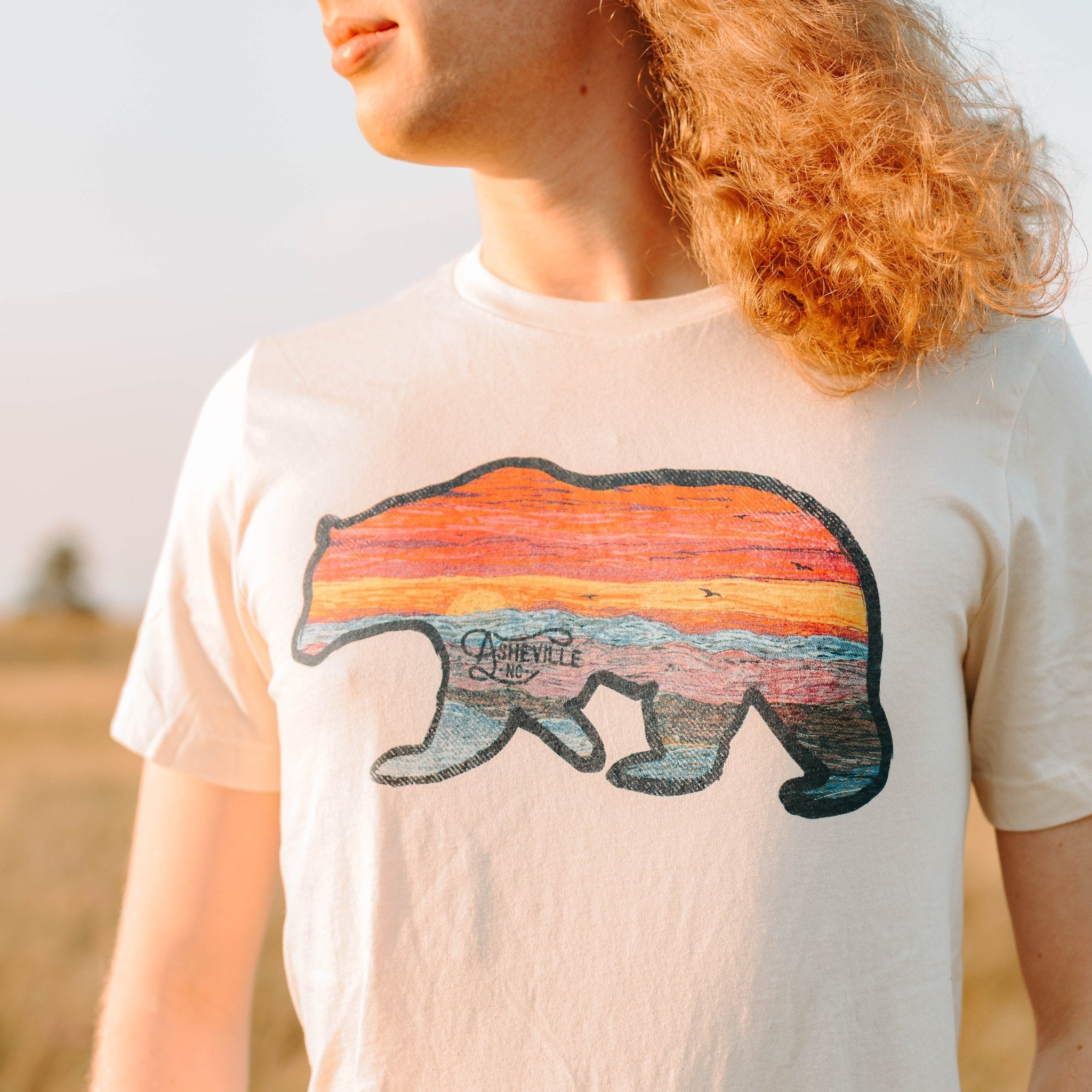 Unisex t-shirt featuring iconic Asheville bear design with rainbow sky