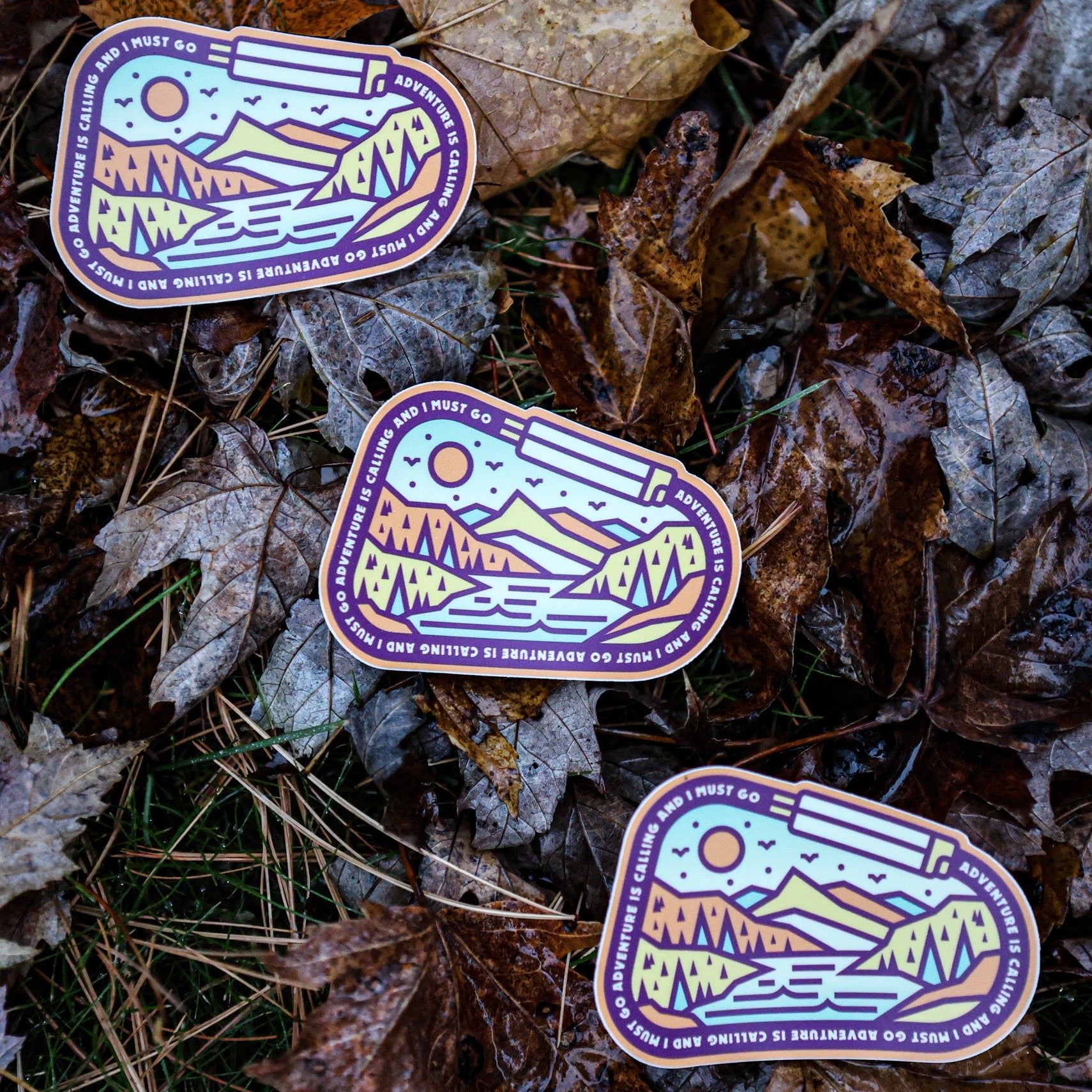 Three identical stickers with a mountain design on a bed of leaves