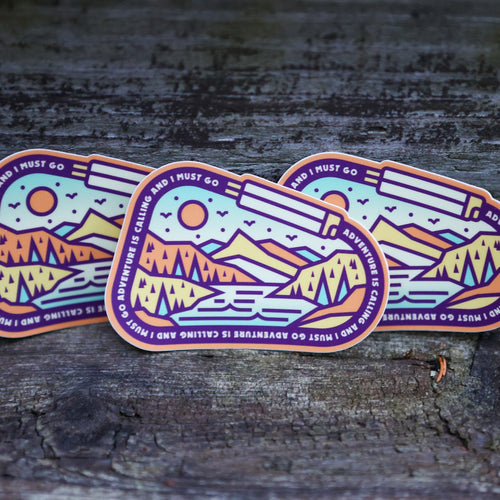 Three colorful mountain-themed stickers on a wooden surface