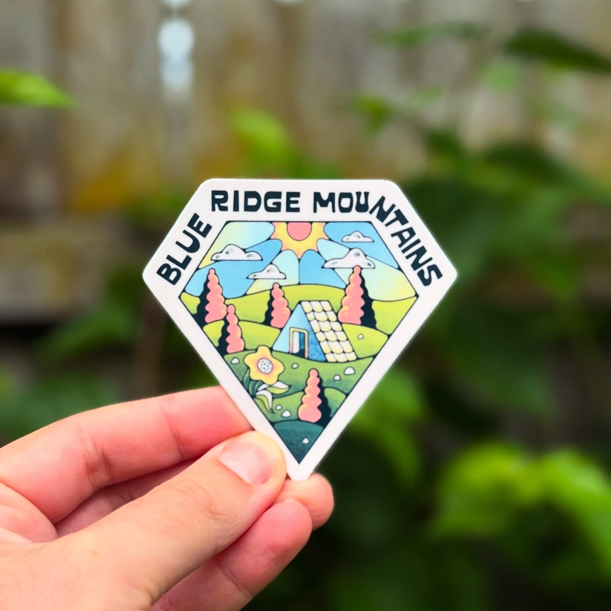 Sticker with 'Blue Ridge Mountains' design held by a hand against a blurred natural background