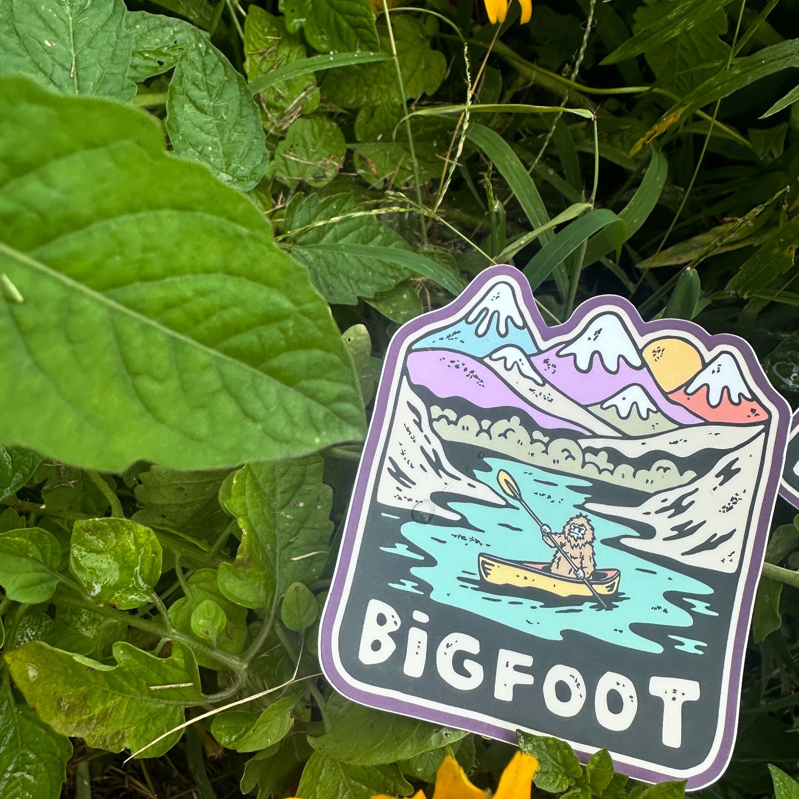 Sticker laying on green foliage, showcasing its natural vibes and vivid detail.

