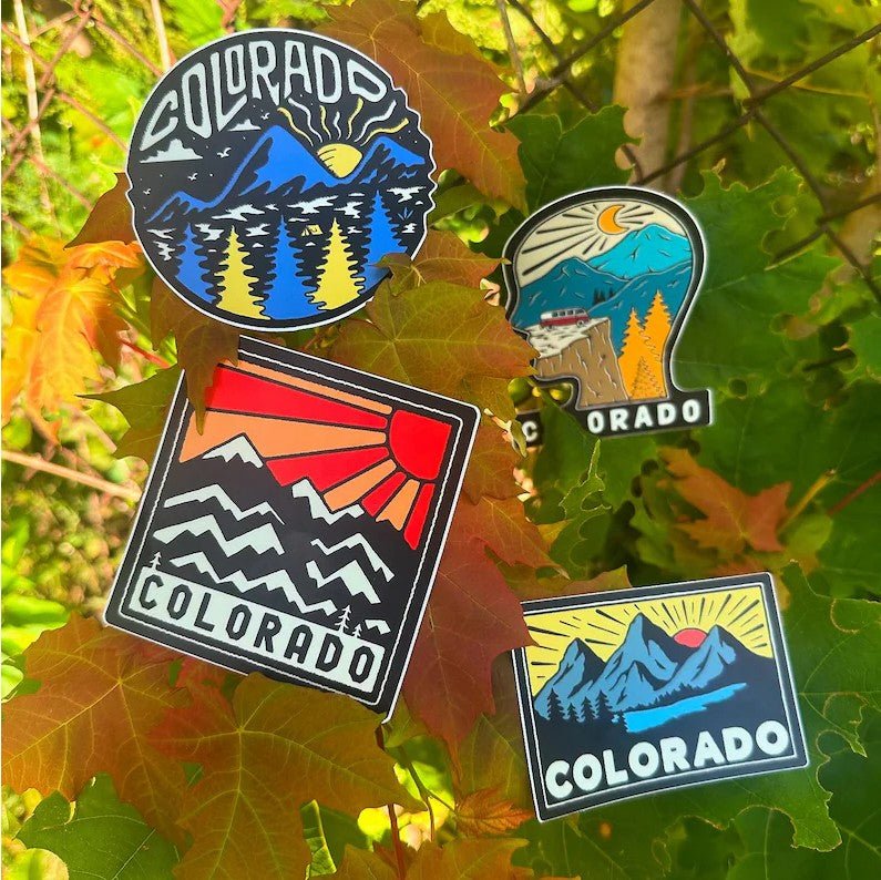 Four Colorado-themed pins on a background of green and orange leaves