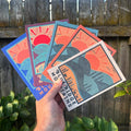 Hand holding five colorful Day Ridge postcards fanned out against wooden fence

