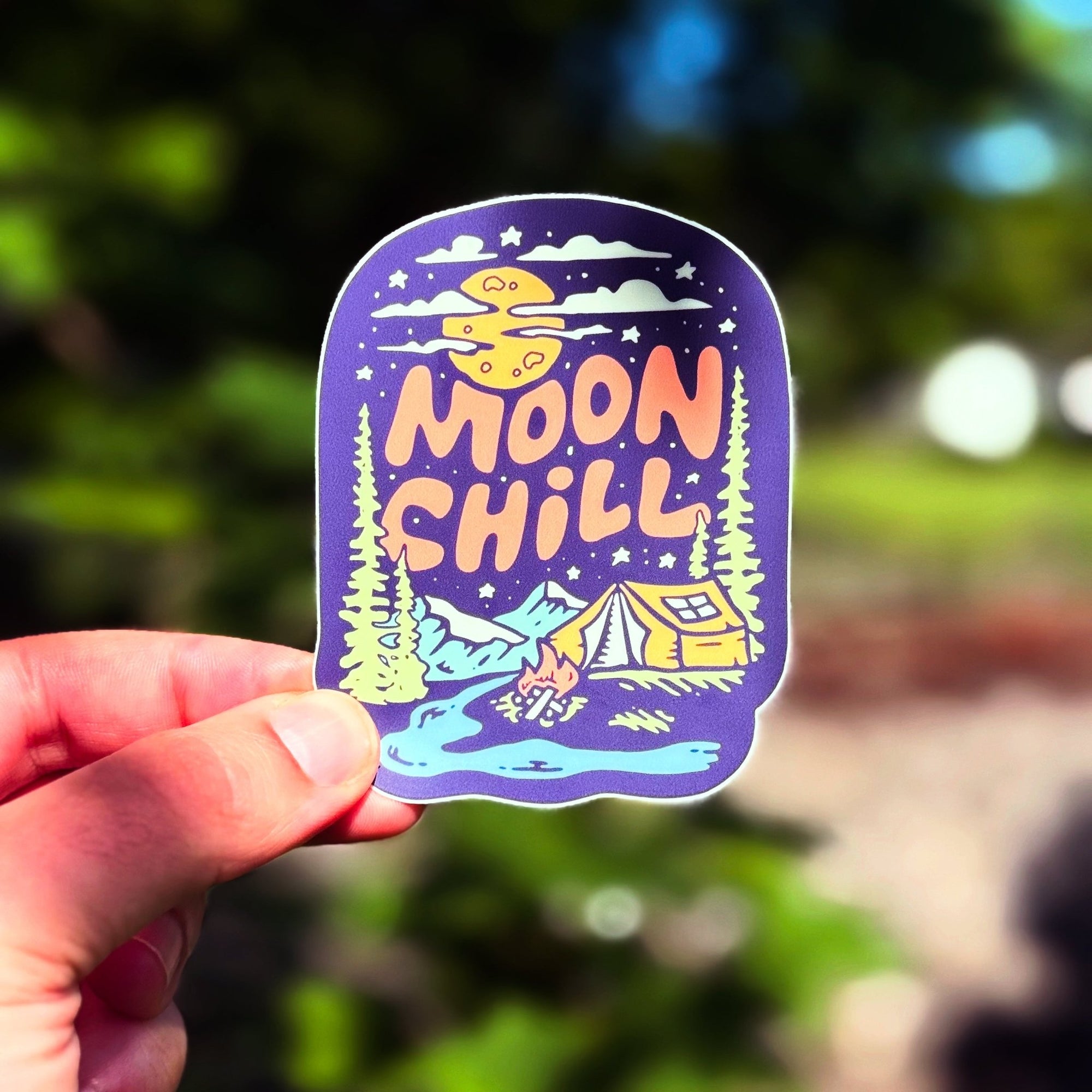 Sticker with 'Moon Chill' design held by a hand against a blurred natural background