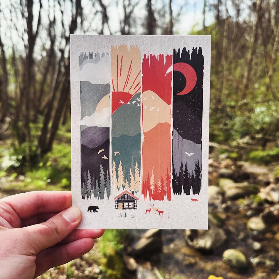 Hand holding a postcard showing four seasonal views of a mountain range, transitioning from foggy morning to sunrise, bright daylight, and a red moon night.

