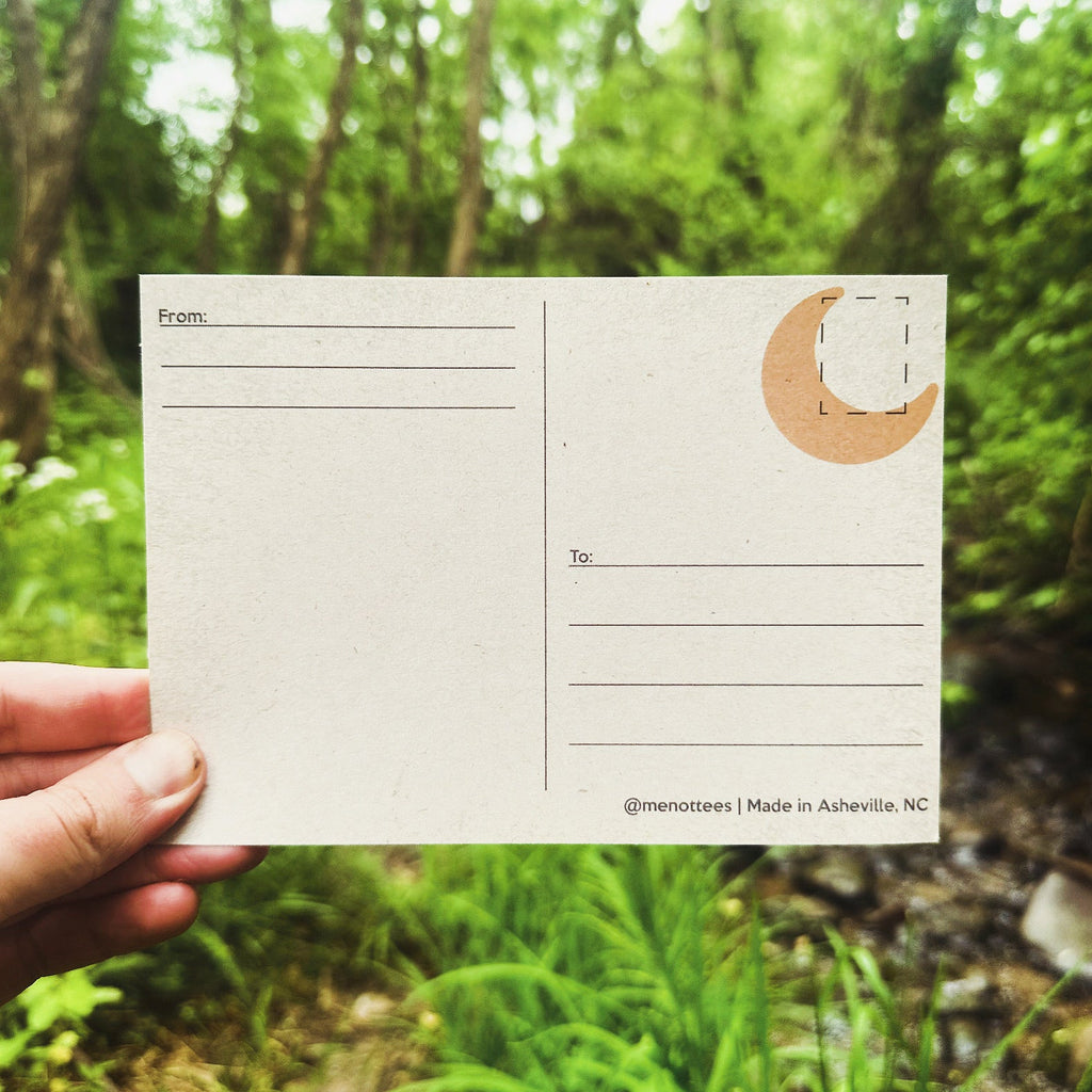 Back of the postcard with a small orange moon design and blank space for writing and postage.

