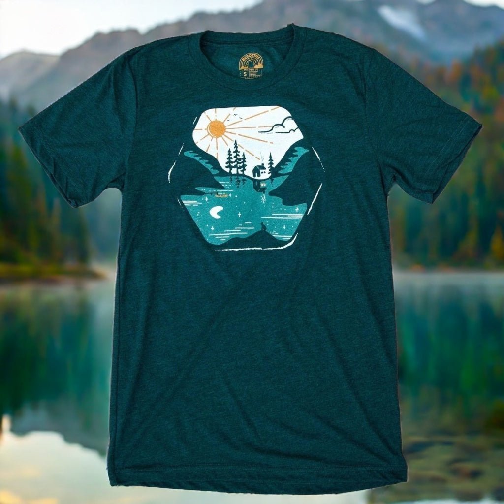 Teal t-shirt with nature graphic design in front of a lake and mountains
