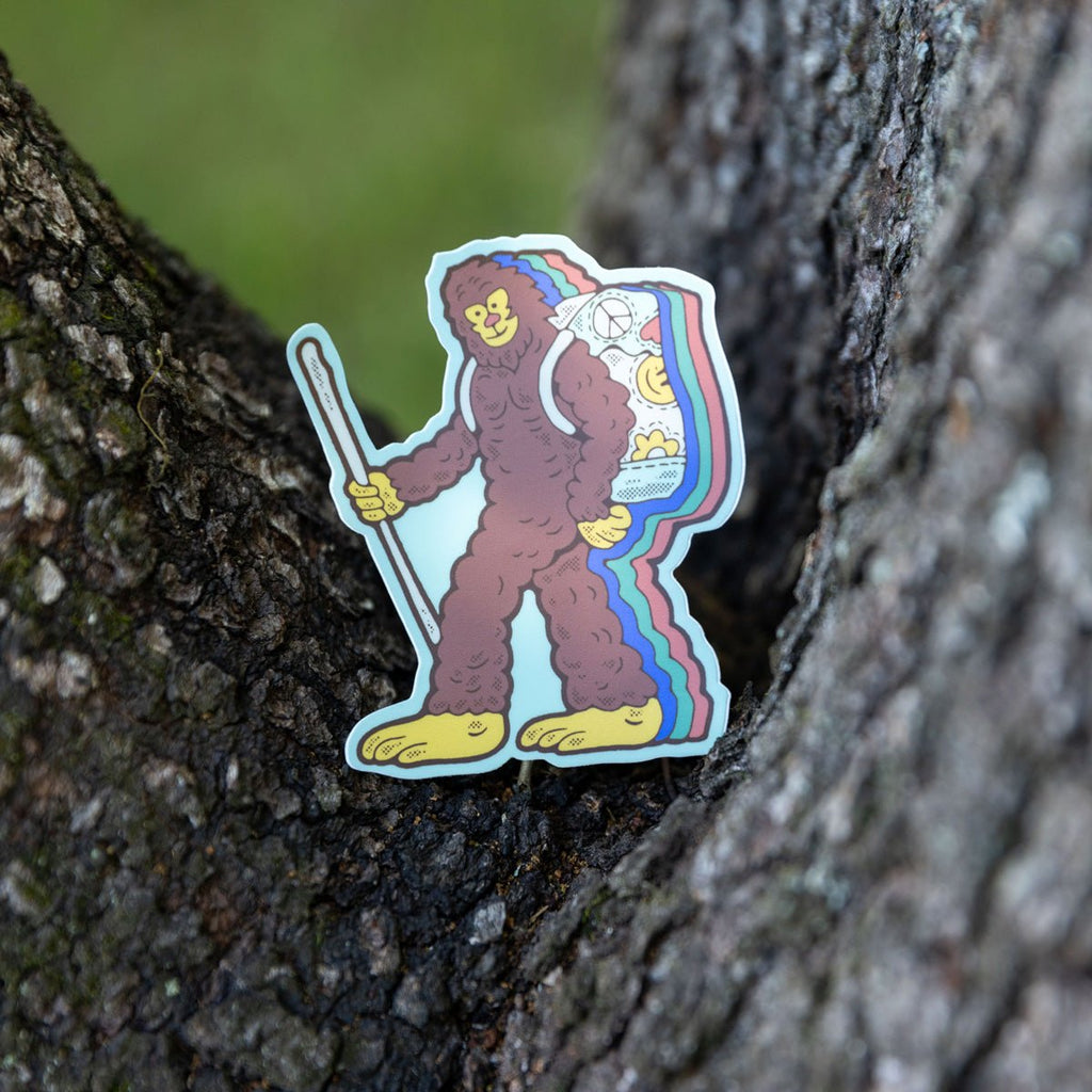 Retro Bigfoot sticker propped against a tree trunk, showing its hiking details.

