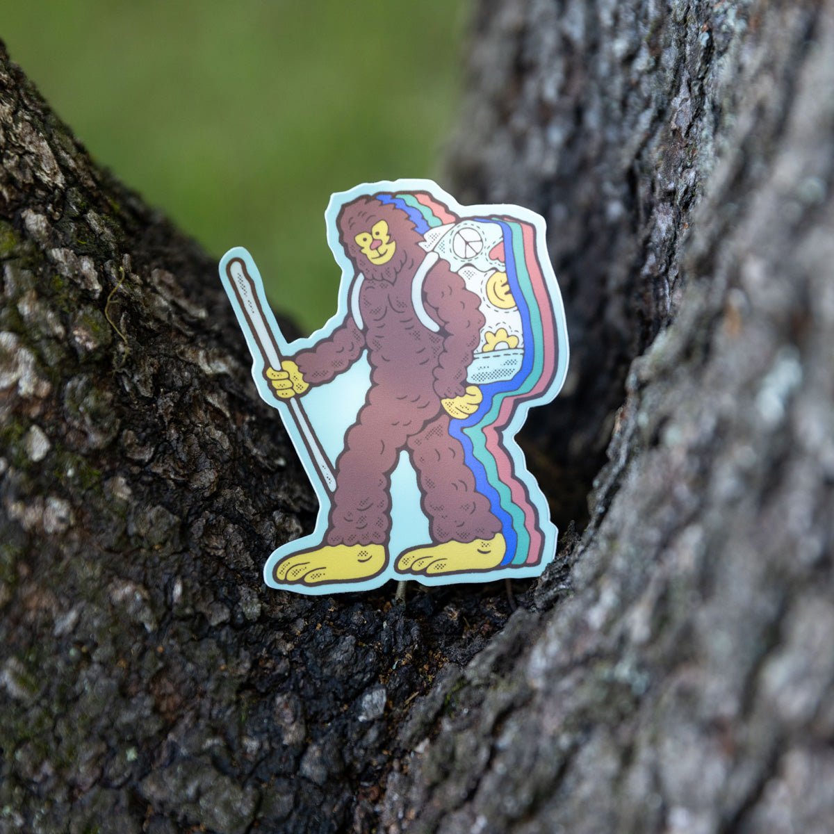 Retro Bigfoot sticker propped against a tree trunk, showing its hiking details.

