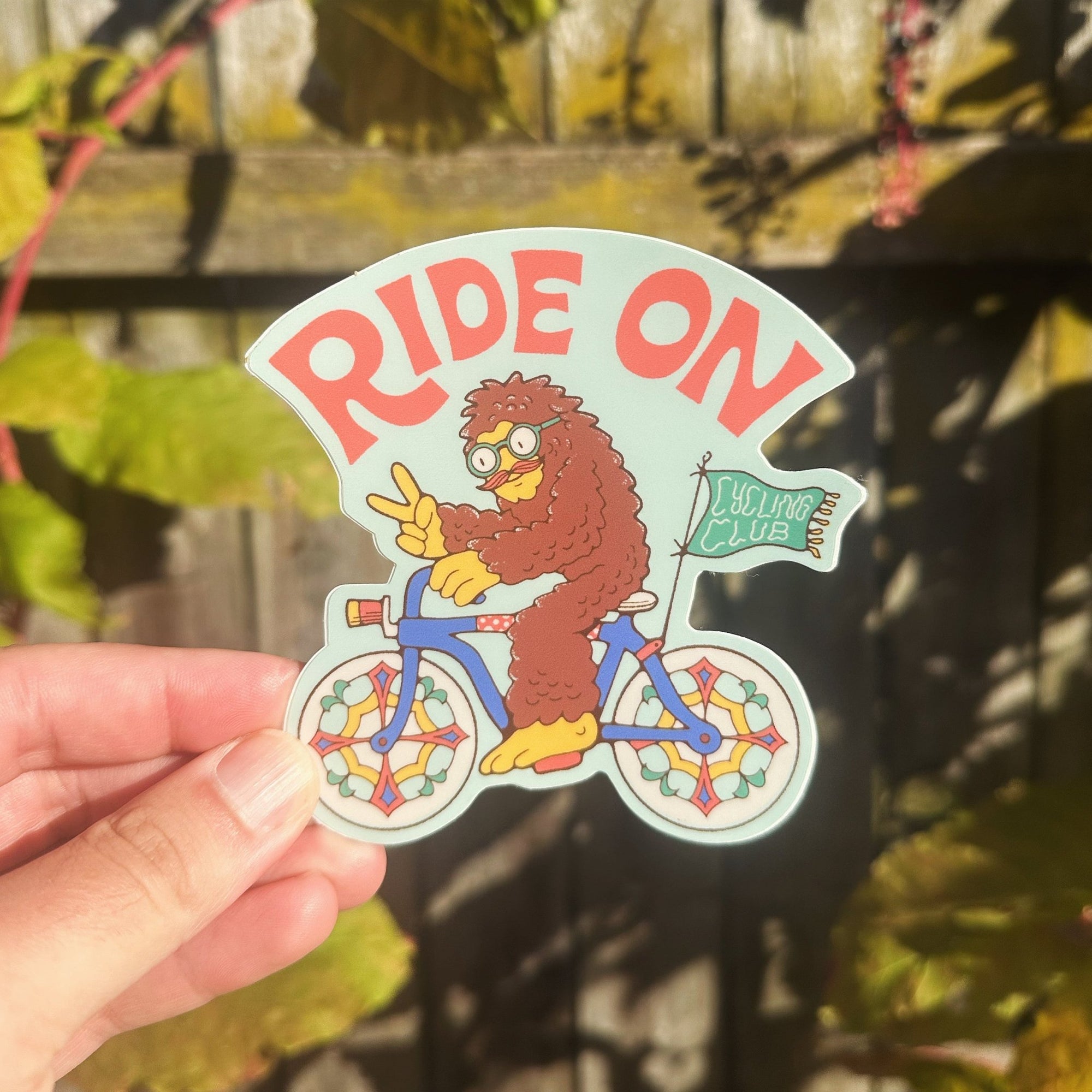 A sticker with an illustration of Bigfoot riding a bicycle and the text 'RIDE ON' above it.