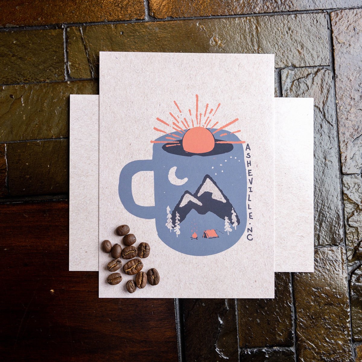 Postcard featuring a coffee mug with a sunrise and mountain scene, surrounded by coffee beans