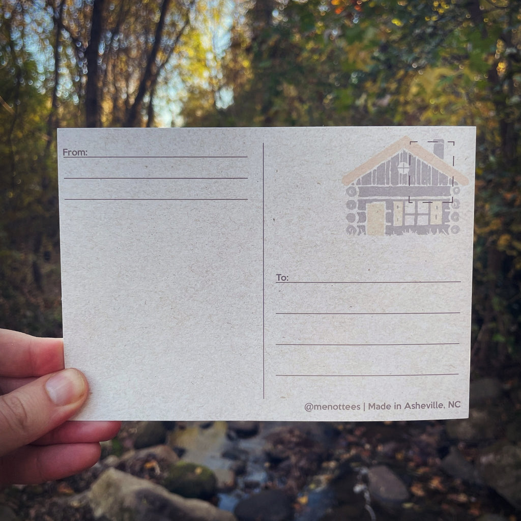 Postcard held in wooded outdoor setting with autumn leaves in background

