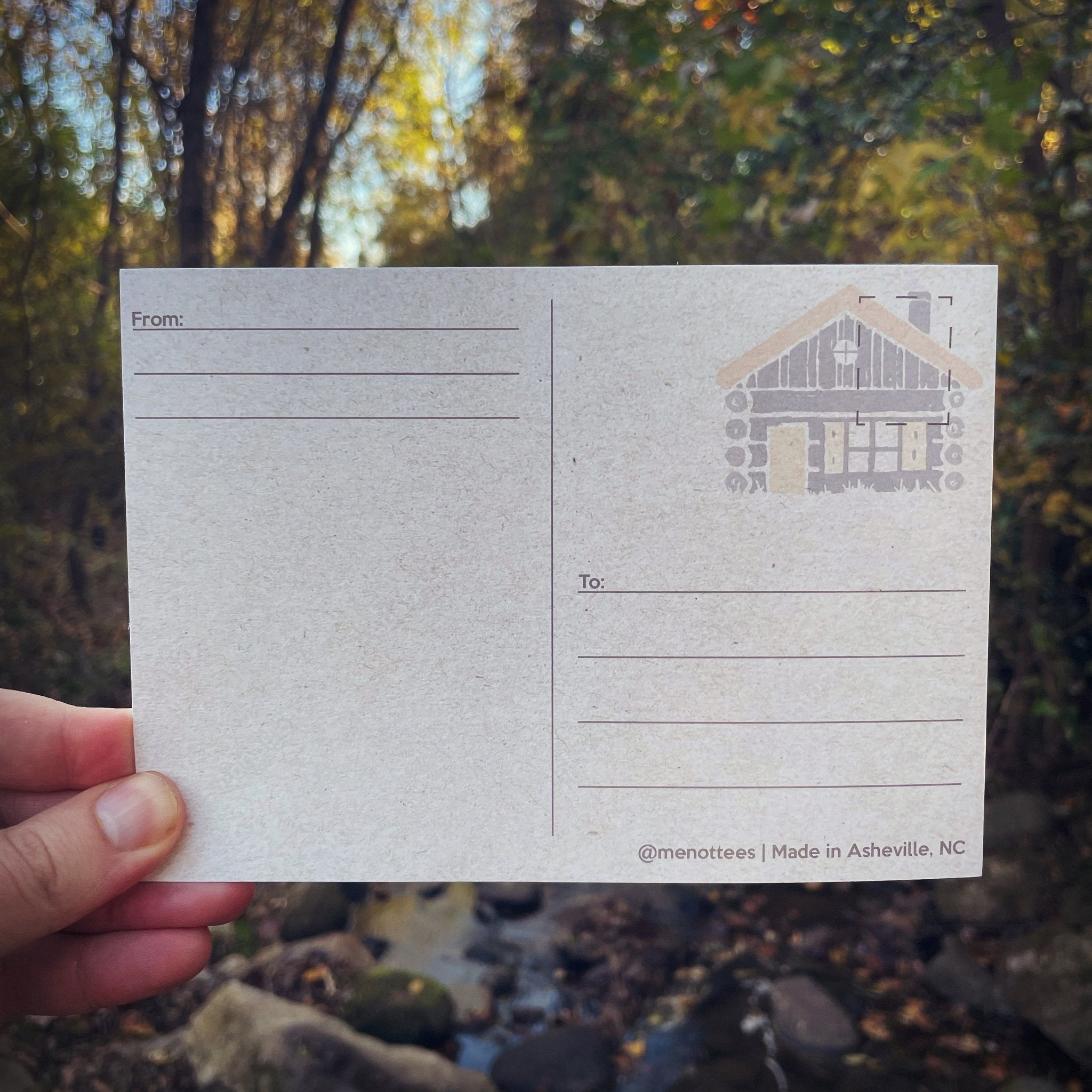 Postcard held in wooded outdoor setting with autumn leaves in background


