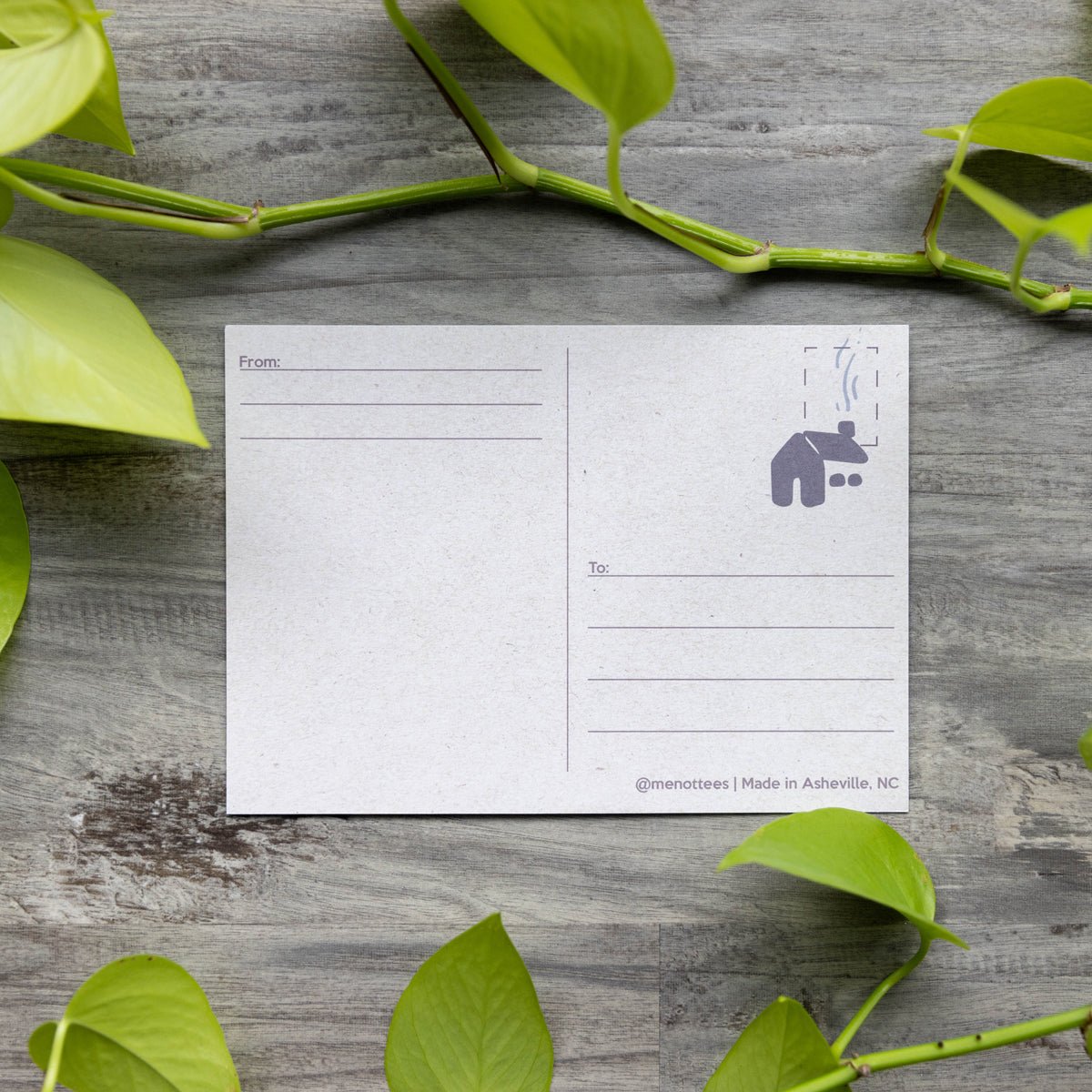 Backside of the postcard displayed on fresh green leaves, showcasing blank space for message, address lines, and stamp placement.

