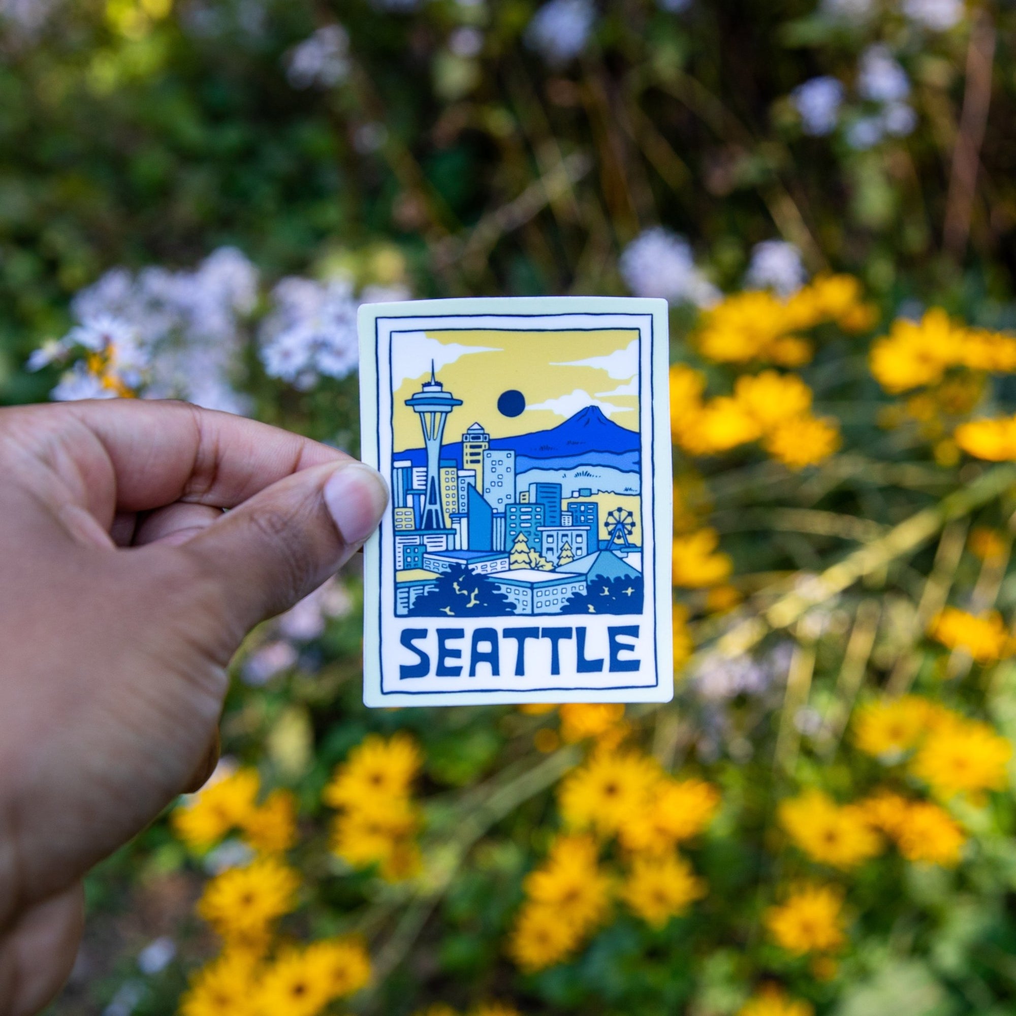 Hand holding Seattle skyline vinyl sticker with flowers in background