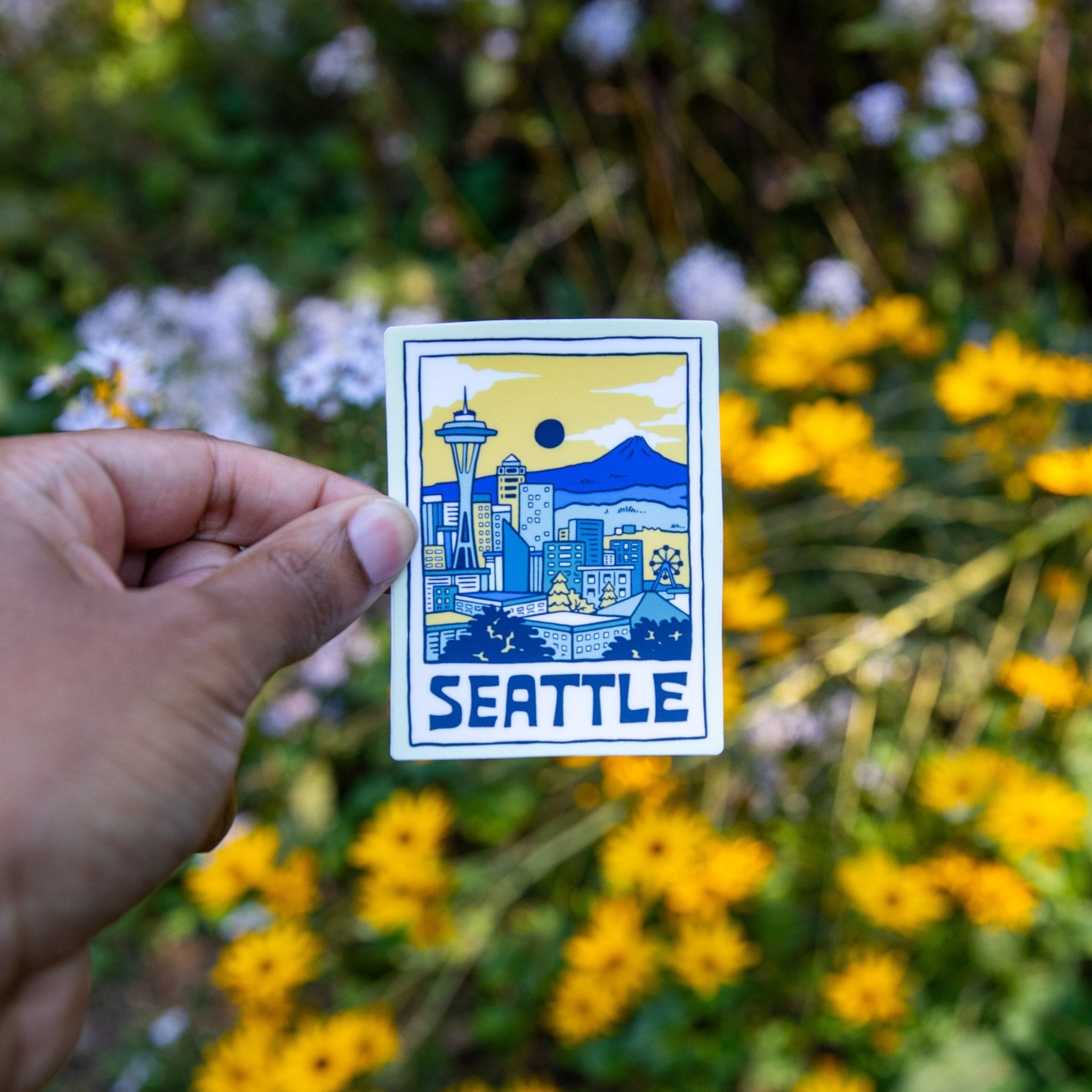 Hand holding Seattle skyline vinyl sticker with flowers in background