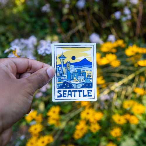 Hand holding Seattle skyline vinyl sticker with flowers in background